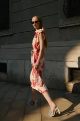 Vestido midi de color beige con estampado floral en tonos rojos y fucsias, con cuello fluido, manga sisa y cinturón del mismo tejido.