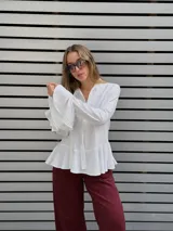 Blusa blanca de textura arrugada, con escote en V y lazos para anudar. Presenta mangas largas con puños acampanados y un diseño con volado en el ruedo.