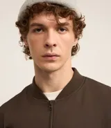 Campera bomber color beige, con cuello alto, cierre frontal con cremallera, bolsillos laterales y puños y cintura elastizados.