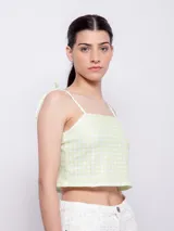 Top corto con escote recto y tirantes finos ajustables mediante nudo en los hombros. Presenta un estampado floral sobre fondo oscuro, con flores rosadas y hojas turquesas.