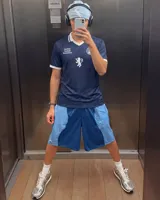 Camiseta de fútbol de Escocia de manga corta, color azul marino con diseño a cuadros sutiles, cuello en V y cuello camisero blanco con líneas azules. Presenta detalles estampados en el frente, incluyendo el escudo de la Asociación de Fútbol de Escocia, un león rampante y el texto 'Scottish Football Association'.