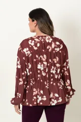 Blusa color marrón con estampado de flores blancas, de manga larga abullonada con puño elástico y cuello redondo con detalle de frunces horizontales.