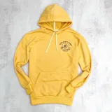 Canguro amarillo con capucha y cordones blancos, bolsillo tipo canguro y estampado frontal con texto y calavera.