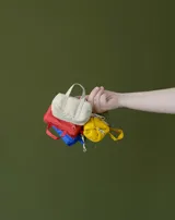 Charm en forma de mini bolso azul, con asas superiores y gancho tipo mosquetón, confeccionado en tela con etiqueta de la marca.