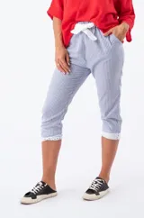 Pantalón capri a rayas verticales azules y blancas con detalle de broderie en el ruedo y lazo de ajuste en la cintura.