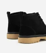 Bota tipo coturno de caña baja confeccionada en cuero gamuzado negro, con cierre de cordones, tirador en el talón y suela track de color tostado.