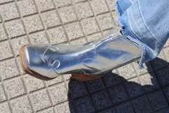 Botas plateadas de cuero con caña media, punta cuadrada, cierre lateral y diseño bordado estilo western.