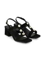 Sandalias de tacón ancho color negro con tiras cruzadas y apliques de botones metálicos dorados en la parte central. Tira ajustable al tobillo con hebilla dorada.
