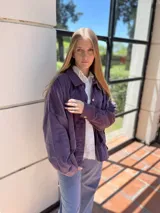 Campera corta de pana color violeta con cuello camisero, cierre frontal con botones dorados, bolsillos de parche en el pecho y corte recto.