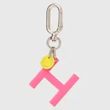 Llavero con dije en forma de letra A color rosado y pequeño dije circular amarillo con logo de la marca grabado. Incluye gancho metálico tipo mosquetón.
