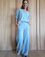 Pantalón de denim estilo palazzo, color azul claro, con cintura elástica en la parte posterior, bolsillos frontales y costuras verticales decorativas a lo largo de las piernas.