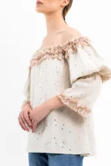 Blusa color crema con pequeños lunares marrones, escote off-shoulder con volados y mangas 3/4 abullonadas con volados en los puños.