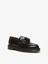 Mocasín Dr. Martens modelo Adrian, color bordó brillante, con borlas y costuras visibles. Confeccionado en cuero Arcadia, con empalmillado Goodyear y suela con cámara de aire resistente.