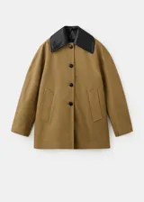 Chaqueta tostada de corte amplio, con cuello camisero grande en contraste de color negro, cierre frontal de botones oscuros y bolsillos laterales discretos.
