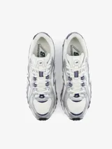 Championes New Balance modelo U204LPC, de estilo inspirados en el running de los años 2000, con capellada de malla blanca y superposiciones metalizadas plateadas con detalles en azul marino.