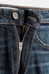 Jeans de tiro medio con diseño baggy barrel, cinco bolsillos y costuras laterales torcidas. Presenta cierre frontal con cremallera y botón metálico.