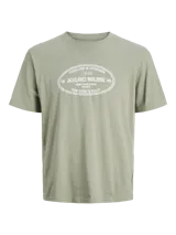 Remera de manga corta y cuello redondo, color verde salvia, con fit relajado. Presenta un estampado frontal ovalado con texto en blanco que incluye "ESTABLISHED IN COPENHAGEN 1990", "JACK&JONES WORLDWIDE MRK", "ORIGINALS CREATIVE DEPARTMENT DAILY BASICS" y "FROM VISION TO REALITY".