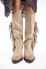 Bota bucanera de caña alta confeccionada en cuero vacuno, con diseño de estilo western que presenta flecos laterales largos y taco cuadrado.