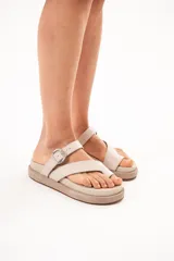 Sandalias de cuero color arena, con diseño de tiras cruzadas, sujetador para el dedo y hebilla metálica lateral. Cuenta con suela acolchada y plataforma plana forrada.