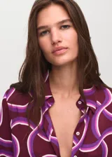 Camisa de tejido fluido color bordó con estampado geométrico abstracto en tonos morados y blancos, cuello camisero, manga larga y cierre frontal de botones.