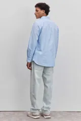Camisa de manga larga en color celeste, con cuello clásico y cierre frontal de botones. Presenta un diseño de corte recto y acabado liso.
