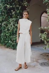 Pantalón fluido de tiro alto en color blanco, con pinzas delanteras, cintura elástica en la espalda y perneras anchas con aberturas laterales pronunciadas.