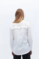 Camisa blanca de algodón con cuello alto con volados y bordado calado en el frente. Tiene mangas largas con puños abotonados y cierre frontal con botones.