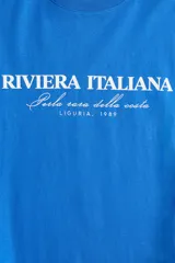 Remera de manga corta, cuello redondo y calce oversize, color azul vibrante, con estampa frontal en blanco que dice "RIVIERA ITALIANA Perla rara della costa LIGURIA, 1989".