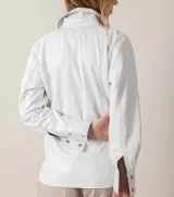 Camisa de cuero ovino italiano color blanco, de corte holgado, con cuello clásico, cierre frontal con broches metálicos, bolsillos laterales y puños con broches.