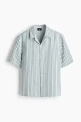 Camisa de manga corta con cuello abierto, confeccionada en una suave mezcla de lyocell. Presenta un diseño a rayas verticales, tapeta lisa y bajo recto con aberturas laterales.