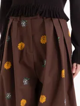 Pantalón de silueta holgada, color marrón, confeccionado en twill de algodón con estampa de flores amarillas y moras. Cuenta con bolsillos laterales y cierre frontal con botón y gancho.