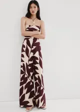 Monopieza sin mangas con escote palabra de honor, de corte recto y largo, con diseño estampado de hojas en tonos beige y bordó. Cuenta con cierre de cremallera en la parte posterior y forro interior.