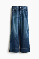 Jean de corte wide leg tiro alto, confeccionado en denim azul con efecto desgastado. Presenta diseño de cinco bolsillos, detalles trenzados a los lados y dobladillo ancho pespunteado.