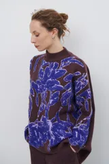 Buzo de tejido de punto con diseño floral en contraste, cuello redondo y mangas largas. Presenta una textura suave y un corte holgado.
