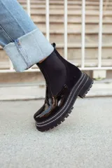 Botas tipo chelsea de cuero negro con textura granulada, paneles laterales elásticos y suela track robusta de goma.