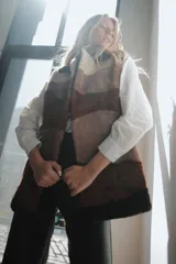 Chaleco largo de piel de oveja con bloques de color en tonos marrón, beige y blanco. Tiene cuello solapa y cierre con un botón forrado en piel.