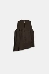 Top de cuello redondo y manga sisa, confeccionado en tejido con acabado satinado. Presenta volantes en cascada y un diseño de bajo asimétrico, con cierre en la espalda mediante pequeña abertura y botón.
