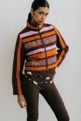 Chaqueta corta con cuello alto y cierre frontal de cremallera. Confeccionada en tejido de lino a rayas horizontales en tonos beige y verde claro, con apliques de galones bordados en tonos dorados y verdes en el pecho y la cintura.