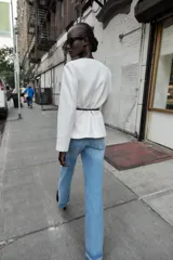 Blazer de textura suave, cuello redondo y manga larga. Presenta un diseño minimalista con cierre frontal mediante un cinturón fino de cuero con hebilla metálica.