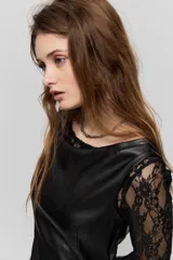 Vestido corto de símil cuero negro, de corte recto, escote amplio y sin mangas, combinado con mangas largas de encaje negro.
