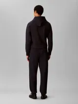 Pantalón de jogging Calvin Klein de felpa color azul marino, con cintura elástica, cordón ajustable, bolsillos laterales y puños elásticos en los tobillos. Cuenta con el monograma CK bordado discretamente en la pierna.