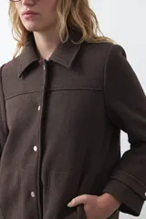 Tapado corto de paño color marrón, con diseño recto, cuello camisero y cierre frontal con broches metálicos. Cuenta con bolsillos frontales.