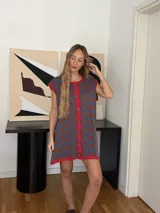 Vestido corto tejido en jacquard de algodón, con diseño a cuadros en tonos azul y marrón, cuello redondo con ribete rojo y cierre frontal con botones.