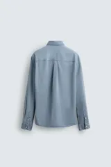 Camisa de corte relajado confeccionada en una mezcla de lyocell y algodón con efecto lavado. Presenta cuello solapa, manga larga con puños abotonados, bolsillo de plastrón en el pecho y cierre frontal con botones.