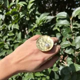 Anillo dorado con base circular texturada y perla plástica engarzada.