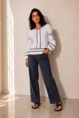 Blusa blanca de manga larga con detalles de bordados florales en tono grisáceo y bandas decorativas en el frente y mangas. Cuenta con cuello redondo y puños elásticos.