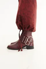 Bota de caña baja confeccionada en cuero con textura crocco, color bordó. Presenta taco cuadrado, punta cuadrada y un accesorio desmontable con doble hebilla metálica y tachas decorativas.