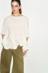 Top de cuello redondo color celeste con textura fruncida, mangas tipo capa y bajo asimétrico.