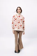 Polera de tejido de punto con cuello alto, diseño holgado y estampado jacquard con motivos geométricos y figuras en tonos beige, naranja y celeste.