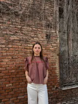 Blusa color chocolate con mangas cortas abullonadas, cuello redondo con volados y detalles de costura en zigzag de color rojo en el pecho y volados oscuros en los hombros.